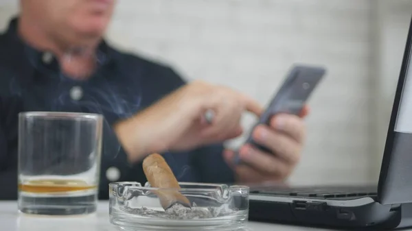 Homályos kép-val egy üzletember dohányzás szivar, Whisky ivás és a Cellpho segítségével — Stock Fotó