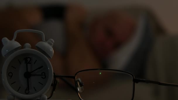 Фокусное переднее изображение с будильником и усталым человеком, спящим на заднем плане — стоковое видео