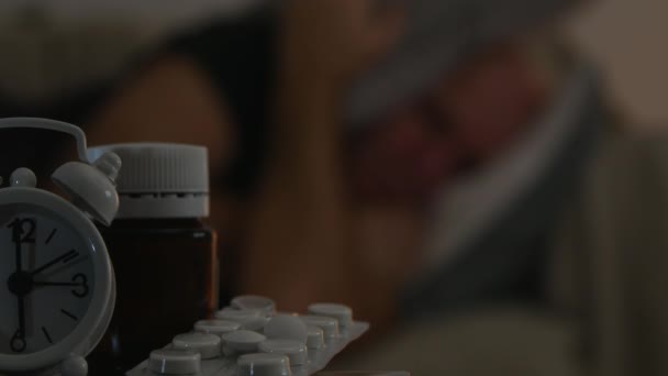 Nemocný muž spí unavená s hodinami a v popředí zaměření lékařské pilulky — Stock video