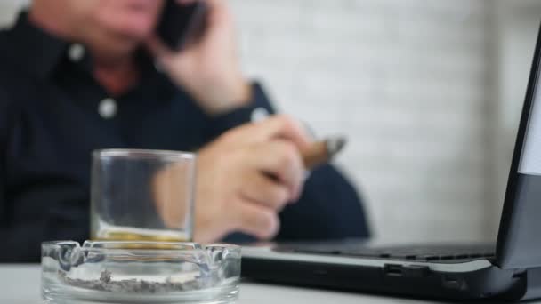 Podnikatel v úřadu mluví o mobilní telefon a kouřil doutník černý — Stock video