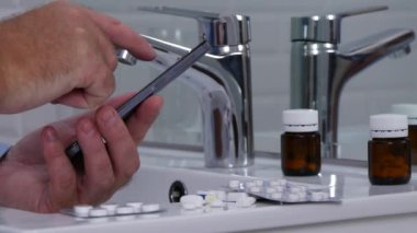 Banyoda lavabonun üzerinde uyuşturucu ve hap ile cep telefonu kullanan adam metin