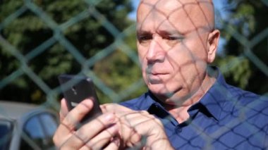 Bir cep telefonu arkasında bir metal çit kullanarak ciddi adam metin