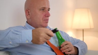 Bıkkın ve yorgun işadamı kanepe dinlenme Tv programı değiştirmek ve bir bira içmek