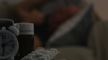 Acı adam yatakta ve ön planda tıp hapları ile bulanık görüntü