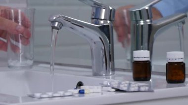 Banyoda adam doldurun bir bardak su ve almak tıbbi hapları ile