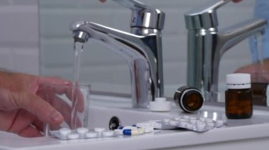 Banyoda adam doldurun bir bardak su ve almak tıbbi hapları ile