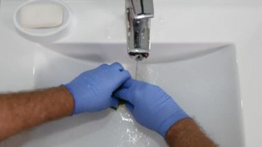 Elinde bir plastik sünger ve deterjan kullanarak lavabo temizlik eldivenli adam