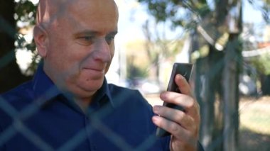 Cep telefonu ve gülümseme kullanarak bir metal çit metin tarafından korunan işadamı