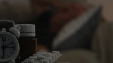 Acı hapları ve çalar saat tablo ile yatakta uyuyan adam