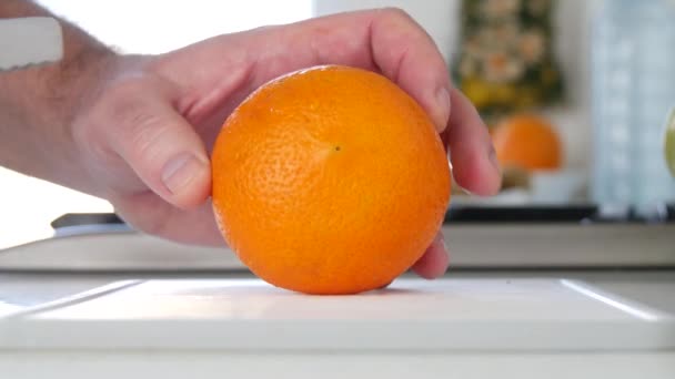 Mann in der Küche schneidet mit Messer eine Orange in frischen süßen und aromatischen Scheiben — Stockvideo