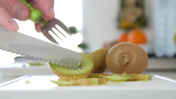 Man skär med en kniv en Kiwi frukt i många skivor för en frukt sallad — Stockvideo