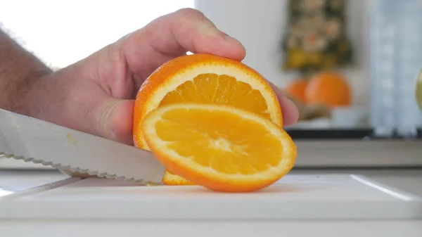 Imagem com as mãos do homem na cozinha cortando em fatias uma fruta fresca e doce laranja — Fotografia de Stock