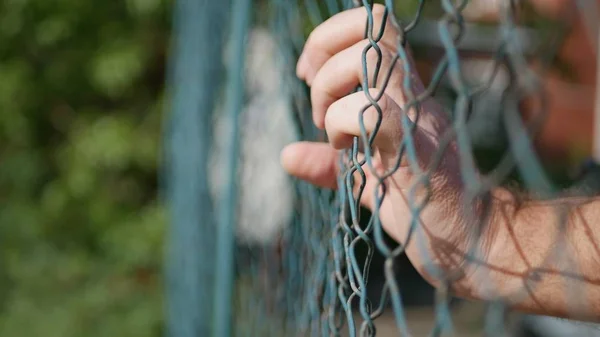 Man handen opknoping in een metalen hek in een beschermingsgebied — Stockfoto