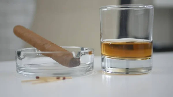 Ízesített fekete dohányzás szivar az Ashtray és egy üveg whisky az asztalon — Stock Fotó