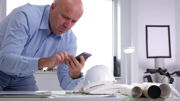 Ingénieur au bureau Parler affaires t un téléphone cellulaire à la recherche de plans techniques — Video