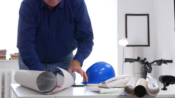 Engenheiro ocupado no escritório interior Abra e analise um plano de construção na mesa — Vídeo de Stock