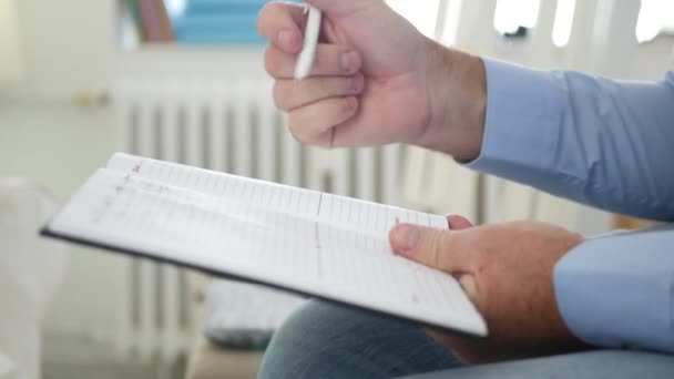 Hombre en el cargo Siéntese y escriba en la agenda Páginas Horario para el próximo día laborable — Vídeos de Stock