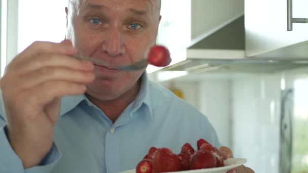 El hombre en la cocina sonríe feliz y come deliciosos sabrosos y dulces frutos de fresa — Vídeo de stock