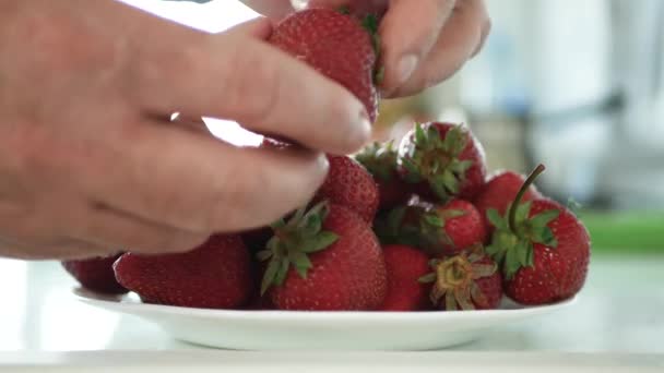 Человек на кухне отбирает и убирает клубничные фрукты на тарелке — стоковое видео