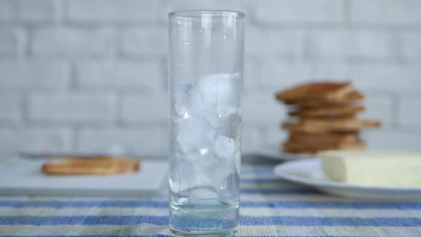 Imagen con un vaso de la mesa de cocina llena de hielo cúbico y agua dulce — Vídeo de stock