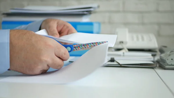 Человек в офисе, сидящий на столе, режет ножницами кусок бумаги — стоковое фото