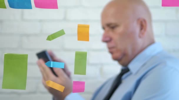 Notas pegajosas coloreadas y hombre de negocios en texto borroso usando el móvil detrás de una ventana — Vídeos de Stock