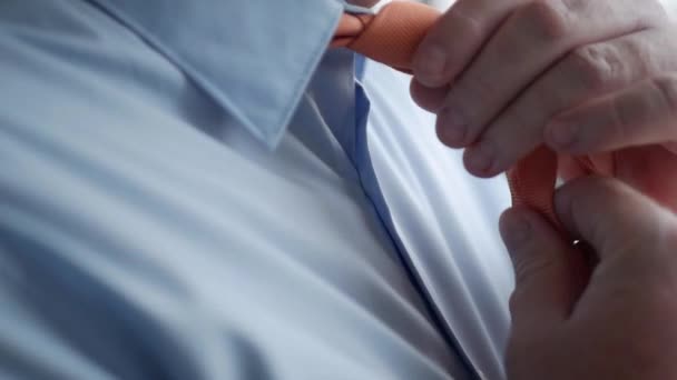Moción lenta con un hombre de negocios elegante que usa una camisa azul y hace un nudo a una corbata anaranjada — Vídeo de stock