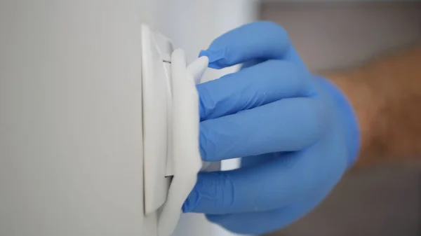 Man Wearing Protection Gloves Cleaning and Disinfecting a Light Switch