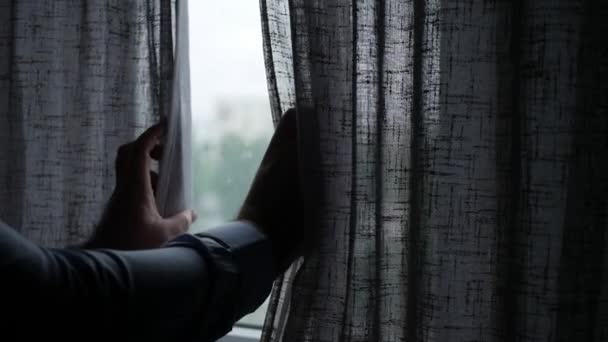 Человек в темной комнате, медленно открывающий оконный занавес солнечным утром, человек в отеле, смотрящий на окно утром — стоковое видео