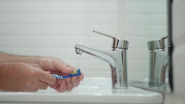 Egy férfi a mosdóban, aki a fogkeféjét mossa vízzel, miután megmosta a fogát. — Stock videók