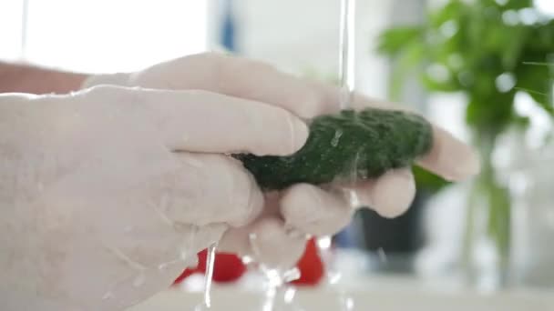Hombre en la cocina con guantes en las manos Lavando un pepino fresco con agua limpia — Vídeo de stock