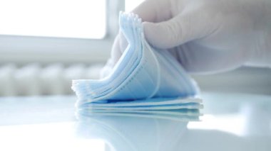 Doktor, hastane odasında cerrahi maske paketini tek tek sayıyor ve kontrol ediyor.