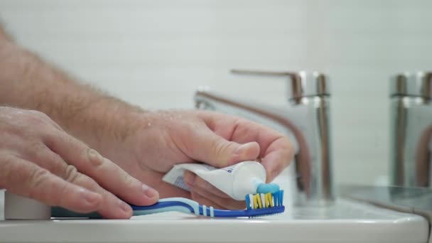 Mann im Badezimmer legt Zahnpasta auf die Zahnbürste, um sich die Zähne zu putzen — Stockvideo