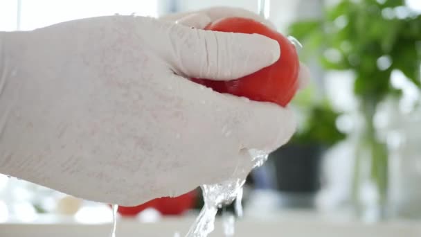 Hombre de cámara lenta en la cocina con guantes en las manos Lave un tomate fresco con agua limpia — Vídeo de stock