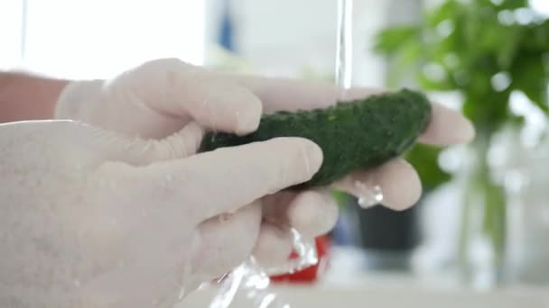 Slow Motion met de man in de keuken met handschoenen aan zijn handen wassen van een verse komkommer met schoon water — Stockvideo