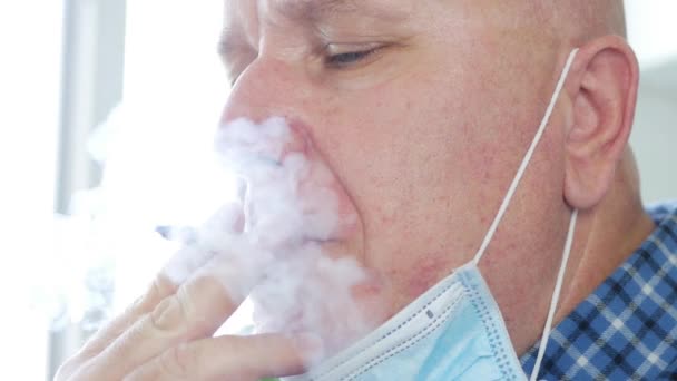 Mann mit OP-Maske im Gesicht raucht entspannt eine Zigarette — Stockvideo