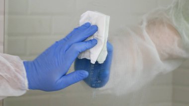 Koruyucu giysiler giyen, tuvalette aynayı dezenfekte eden, karantina altındaki bir hastanedeki tuvaletin içini temizleyen...