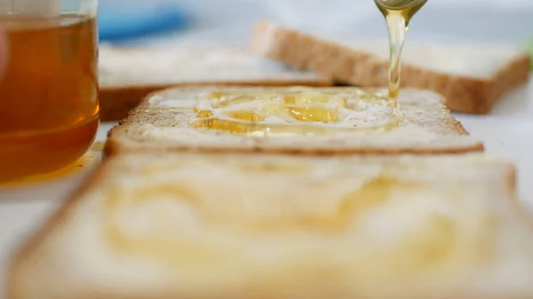 Café da manhã com homem espalhando mel doce no brinde, mel fresco em uma fatia de pão na cozinha — Fotografia de Stock