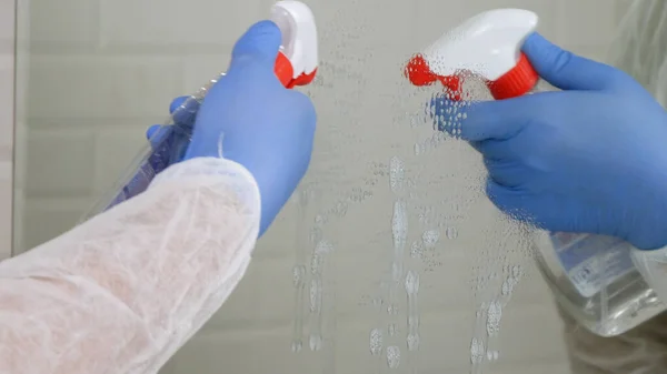Persona que usa ropa de protección desinfectando un espejo en un baño, limpiando el interior de una habitación de baño en un hospital en cuarentena — Foto de Stock