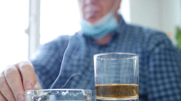 Αναστατωμένος άνθρωπος με προστατευτική μάσκα στο πρόσωπό του Ποτό αλκοόλ και καπνού ένα τσιγάρο — Αρχείο Βίντεο
