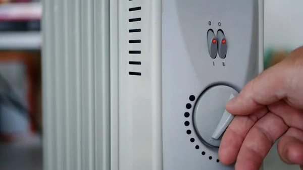Man Sets the Heating Temperature of an Electric Radiator at Home in a Cold Room