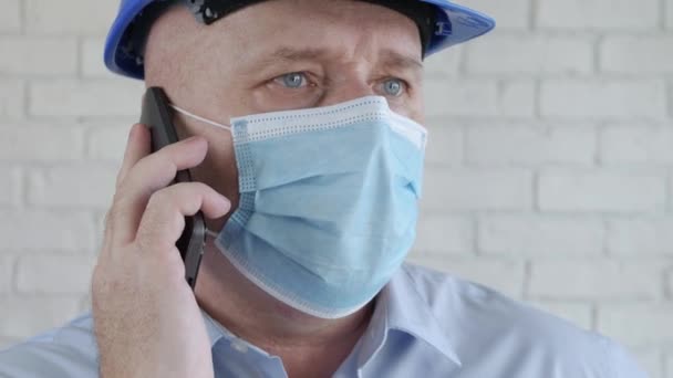 Engenheiro com capacete de segurança e uma máscara de proteção em seu rosto conversando com o telefone celular — Vídeo de Stock