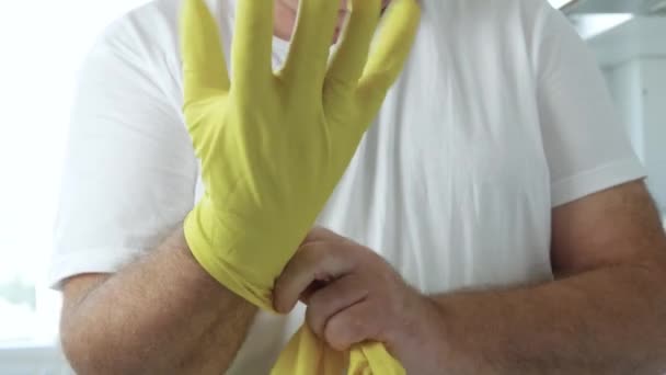 Чоловік наносить свої жовті захисні рукавички на руки готуючись почати прибирати на кухні та у ванній — стокове відео