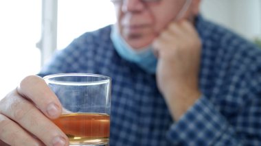 Yüzünde koruma maskesi olan sarhoş bir adam bir barda alkolle içki içiyor.