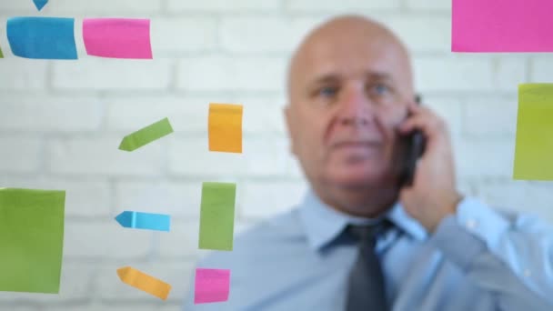 Imagen borrosa con un hombre de negocios hablando con el teléfono móvil y haciendo gestos en la parte posterior de un tablero transparente con notas adhesivas — Vídeos de Stock