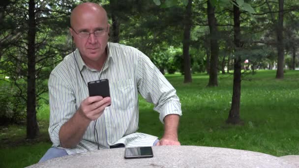 Sénior no Parque Relaxa Ouvindo Música de um Smartphone com Auscultadores — Vídeo de Stock