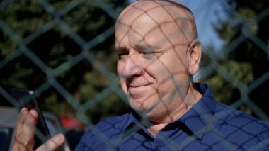 Metalik Çitin Arkasında Akıllı Telefon Kullanan Yaşlı Bir Kişi Görüntü