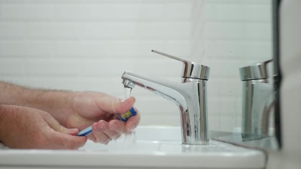Медленное движение человека в ванной комнате чистить свою зубную щетку водой после того, как он почистил зубы — стоковое видео