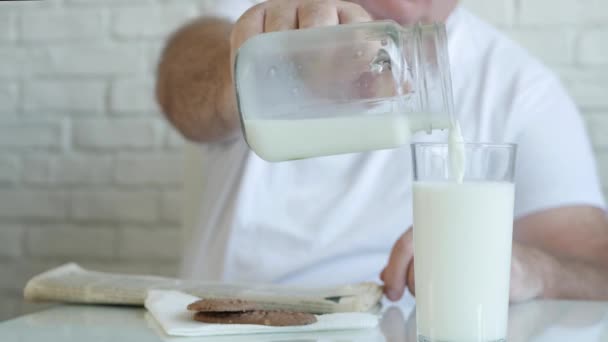 Eine Person liest eine Zeitung und füllt ein Glas mit frischer Milch zum Frühstück, genießt ein schmackhaftes und voll mit Vitaminmilch — Stockvideo