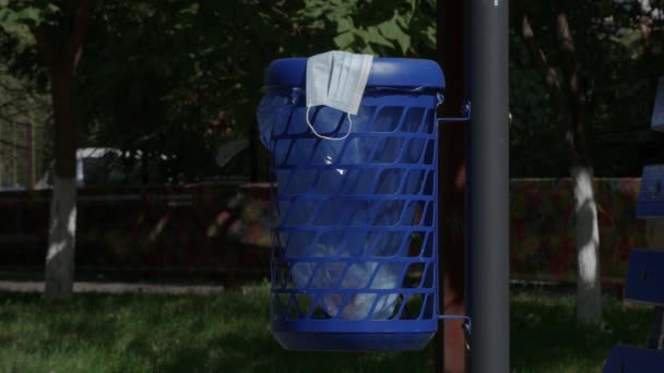 Медицинская маска для лица, брошенная в мусорную корзину на улице, опасный мусор, зараженный коронавирусом — стоковое видео